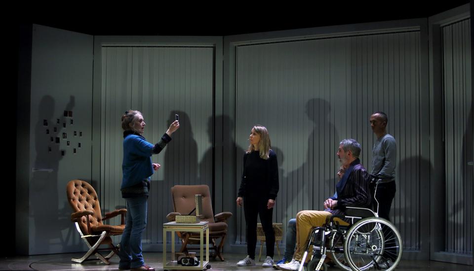 Des personnes dans une pièce. Une femme montre une photo, les autres, dont une personne en fauteuil roulant, regardent.